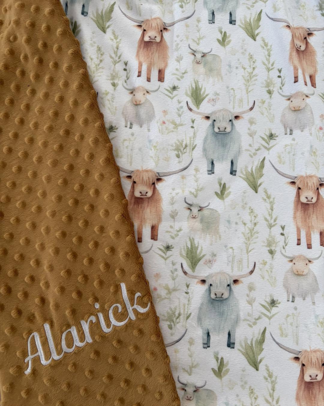 Close-up of a blanket: Highland cow print fabric, mustard Minky and the embroidered name Alarick